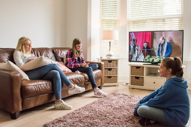 Three people sat in a cosy living room watching TV