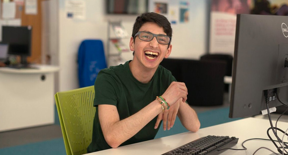 An image of a young man smiling sitting at a desk