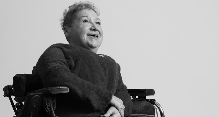 An image of Clare gray, she wears a jumper has cropped hair and sits in her powered chair