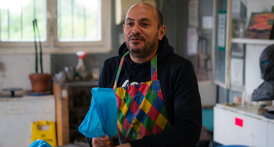 An image of a man wearing an apron, working with clay in an art studio