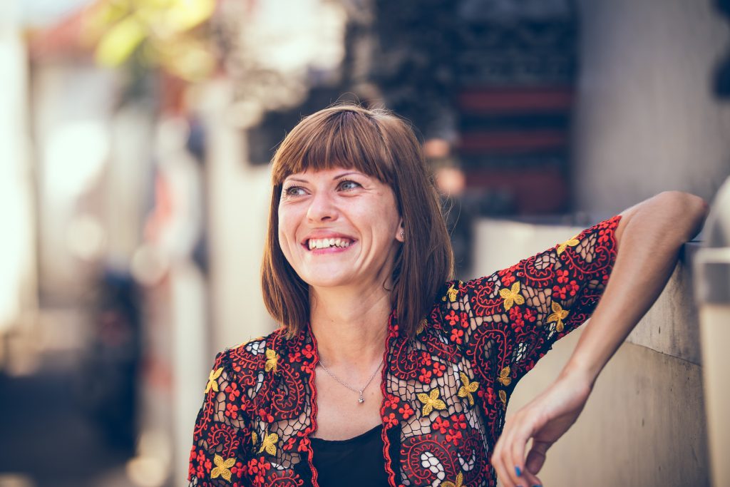 An image of a woman with a flowery shirt who leans against a wall